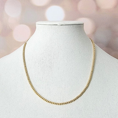 Minimalist gold bead necklace on a display.