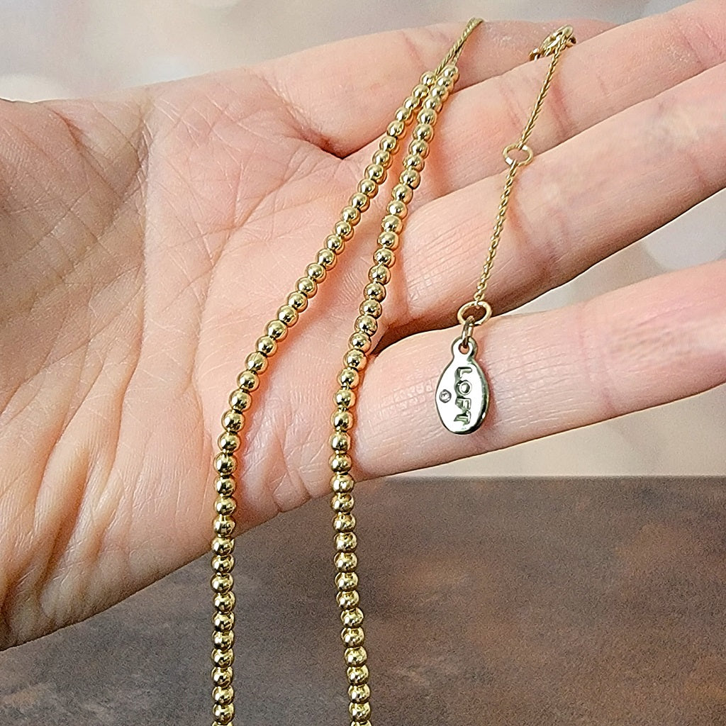 Minimalist gold beaded necklace in hand.