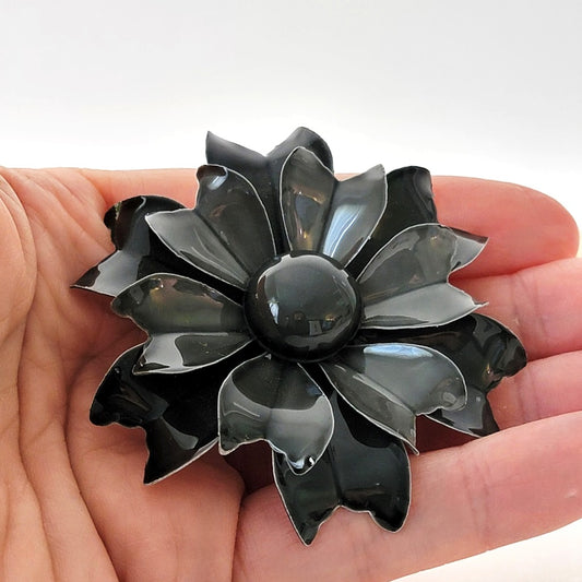 Black enamel flower brooch in hand.