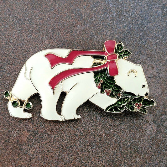 White enamel polar bear Christmas pin, with a red bow and holly wreath around its neck.