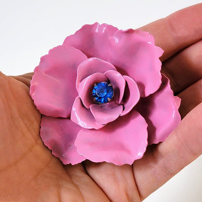 Pink and blue vintage flower pin in hand.