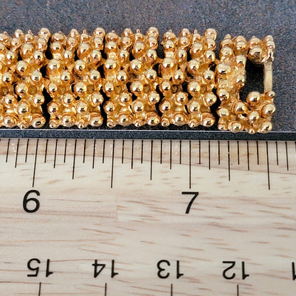 End of a gold tone bracelet next to a ruler.