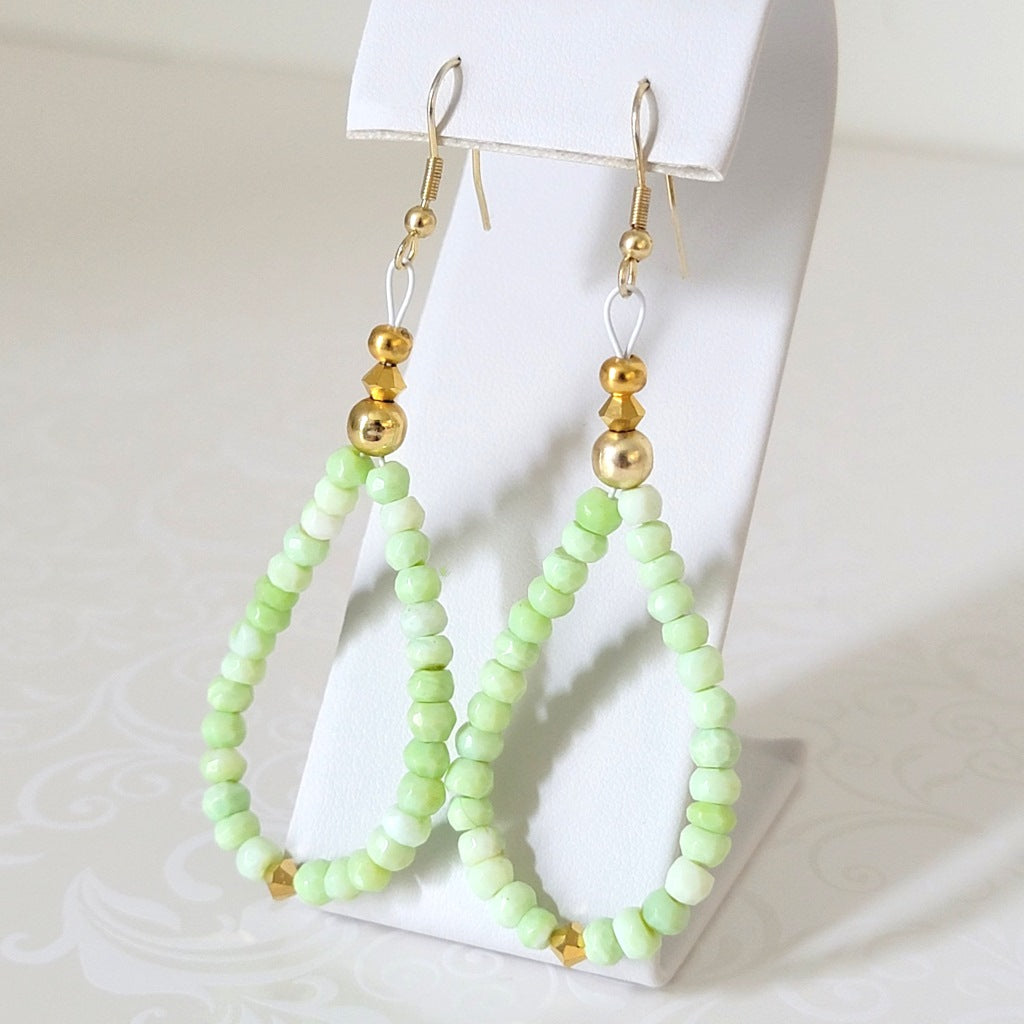 Green opal beaded dangle earrings, with gold crystal accents, shown on a display stand.