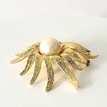 Faux pearl center of a vintage gold tone floral brooch.