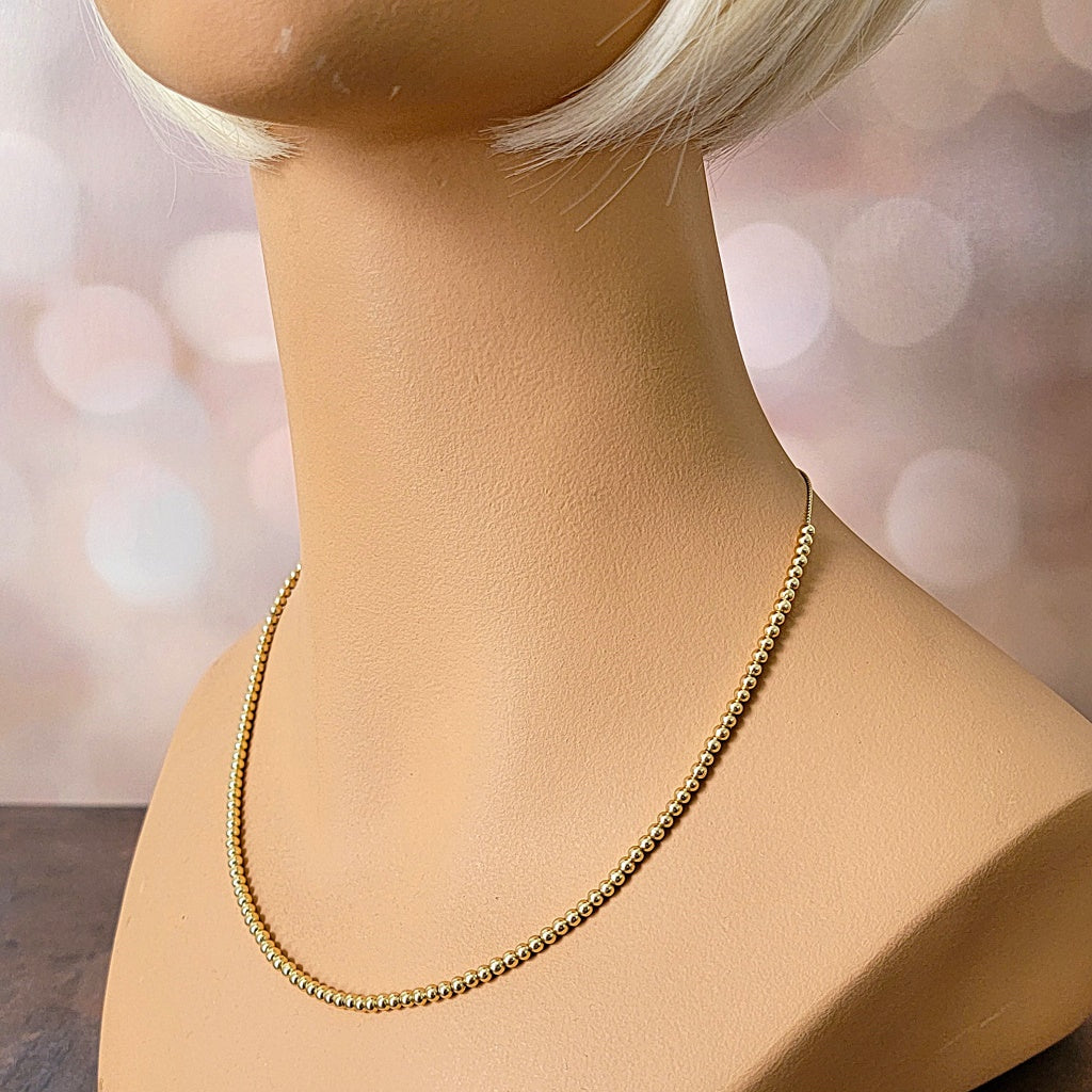 Gold tone small, beaded necklace on a mannequin.