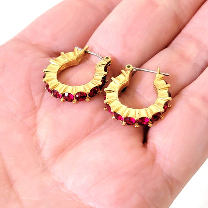 Napier gold tone and red rhinestone hoop earrings, shown in hand, for size comparison.