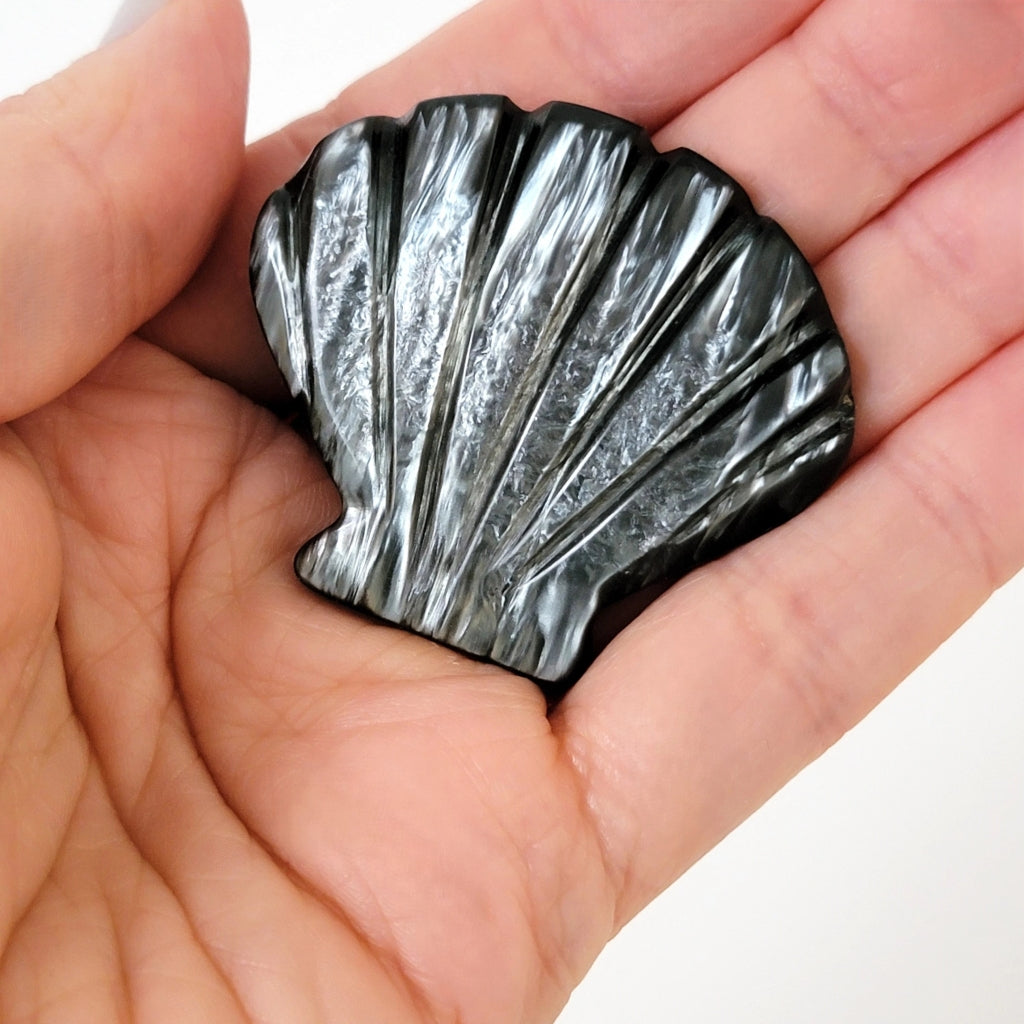 Iridescent carved gray plastic shell pin in hand.