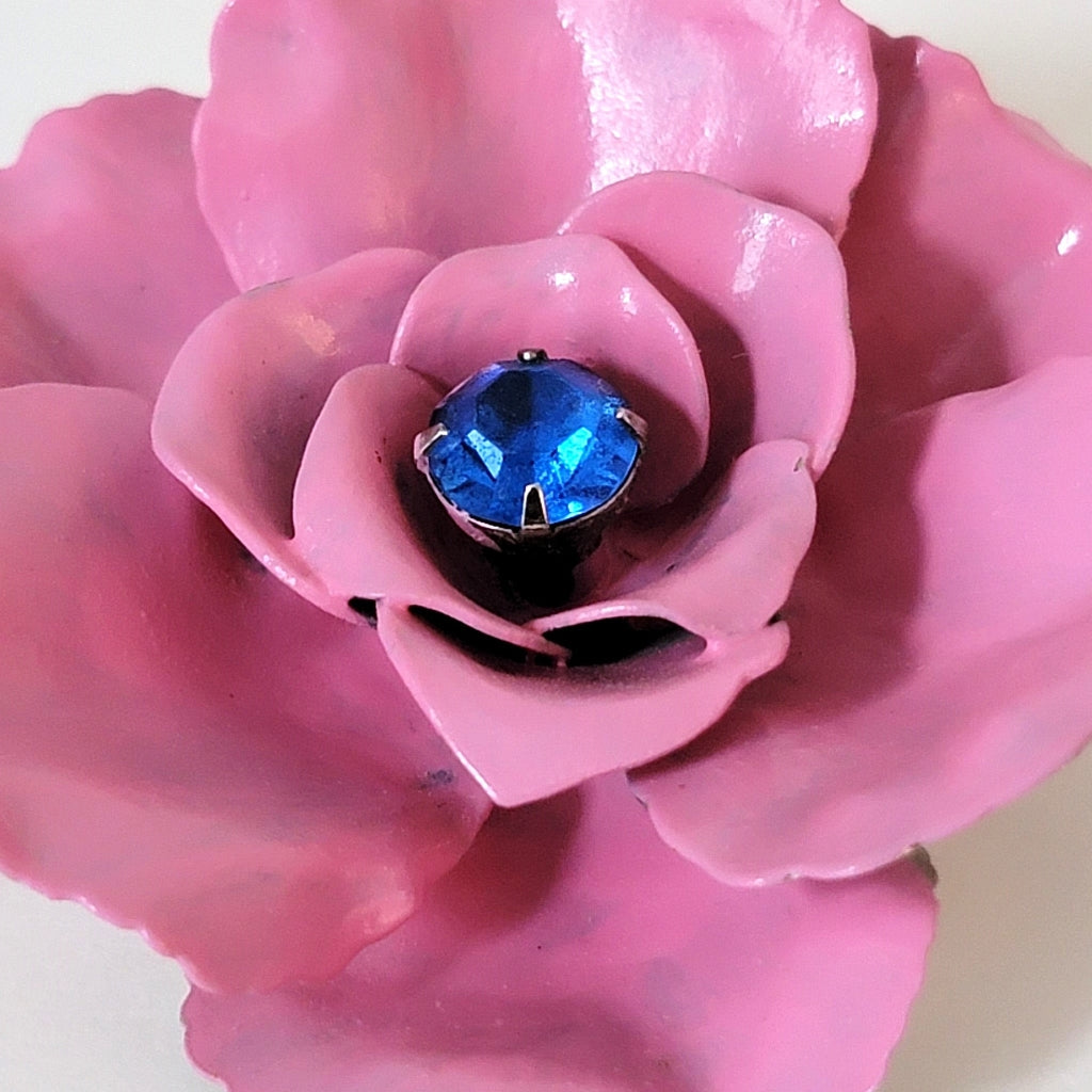 Blue rhinestone inside of pink enameled metal petals.