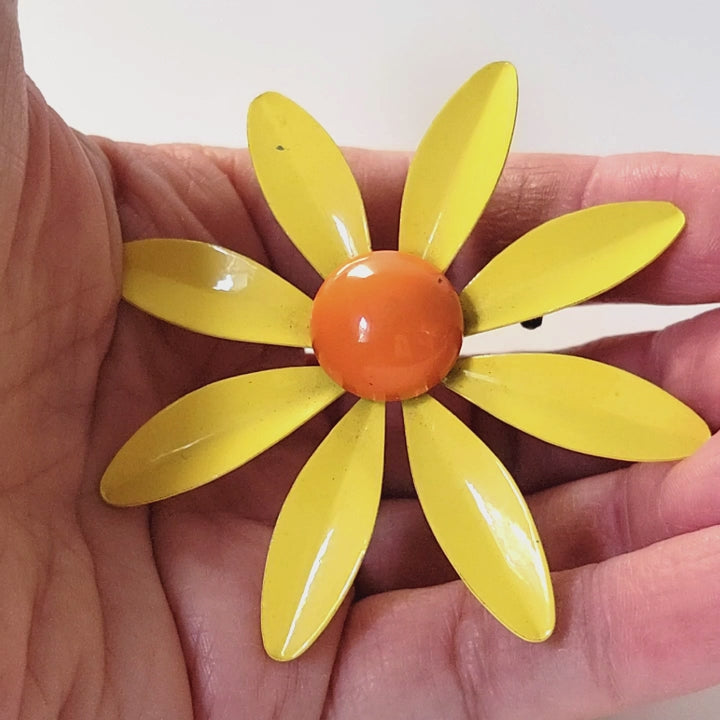 Yellow enamel flower brooch in hand.