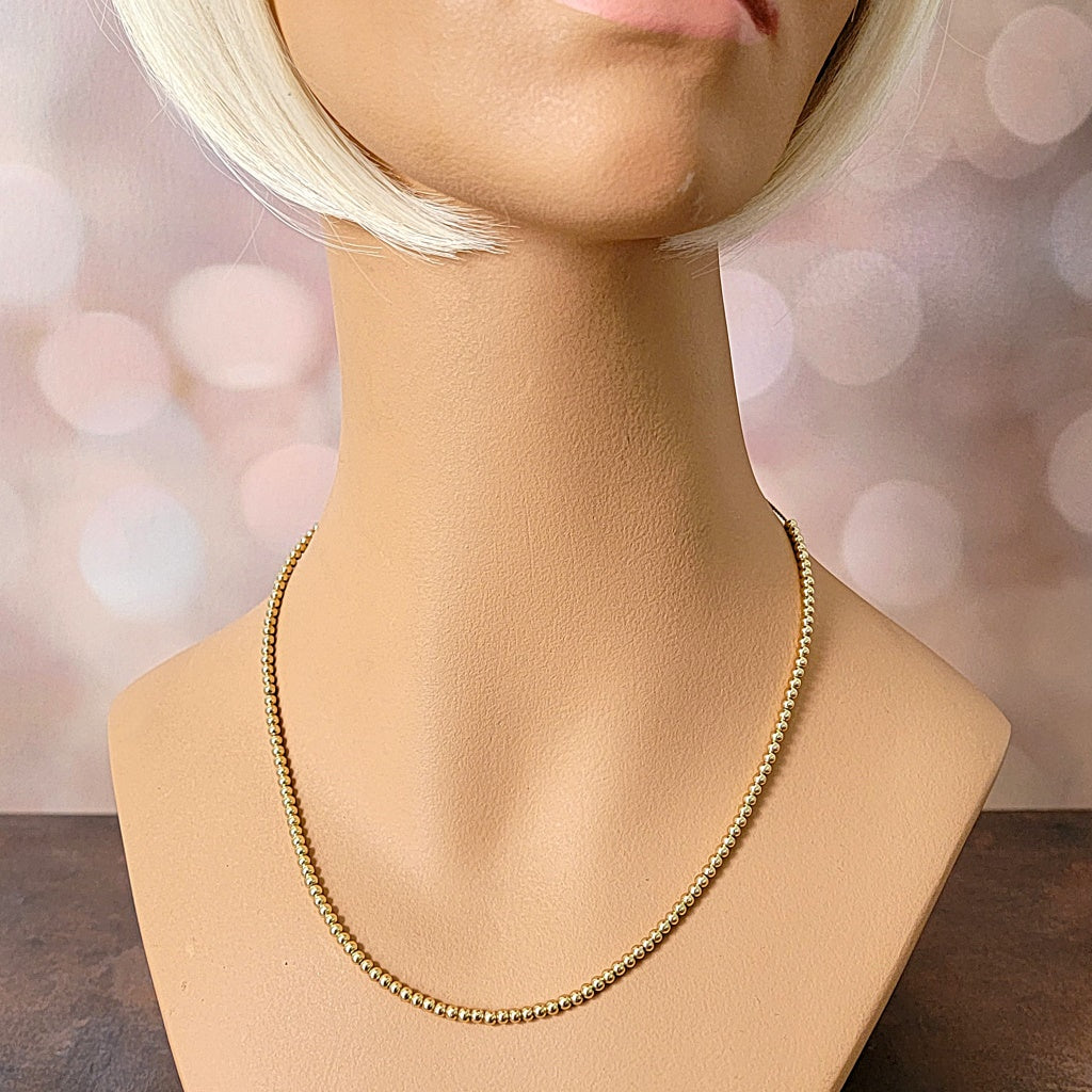 Skinny gold tone beaded necklace on a mannequin.