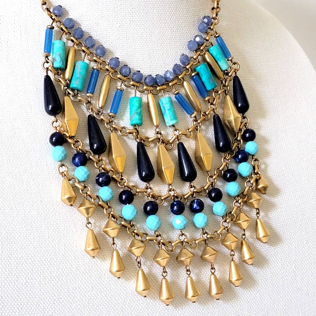 Boho faux turquoise and gold tone bib necklace, shown close-up, on a display stand. Signed Stella.